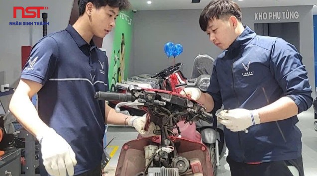 Hai kỹ thuật viên tháo lắp bộ phận xe máy điện trên bàn làm việc
