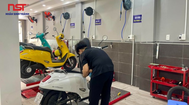 Kỹ thuật viên kiểm tra xe máy điện màu vàng trong xưởng dịch vụ
