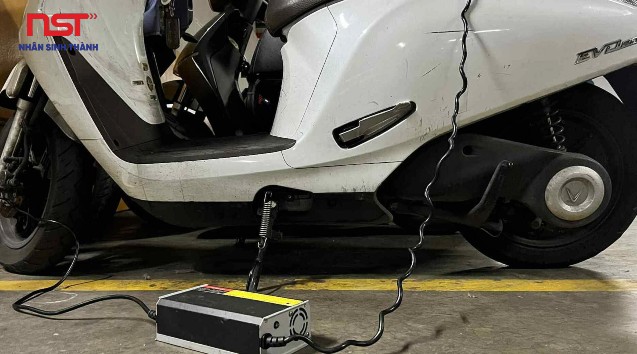 Xe máy điện màu trắng đang cắm sạc bằng bộ sạc rời